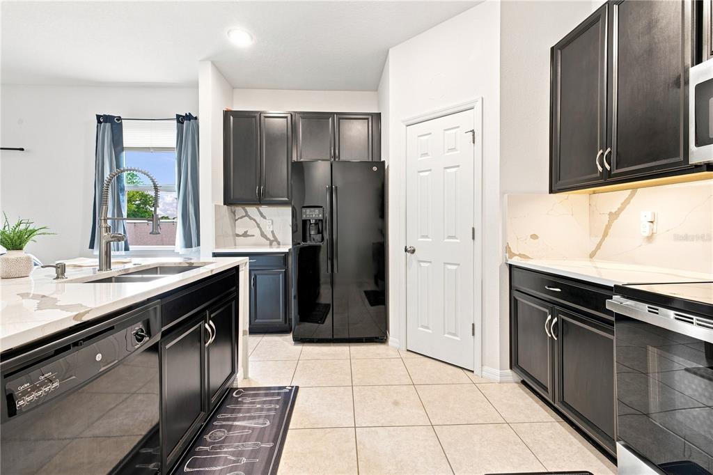 A kitchen features dark cabinetry, stainless steel appliances, a white island, and light tile flooring — 1045 DUDLEY DRIVE, KISSIMMEE, FL