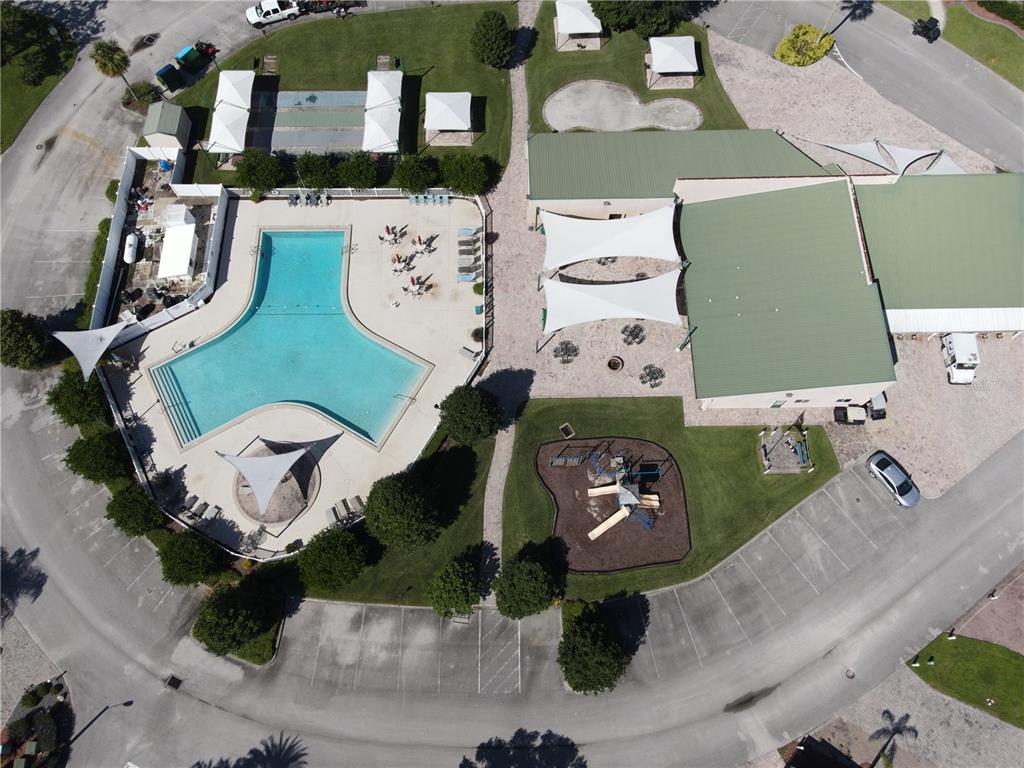 Aerial view of a community recreation area featuring a swimming pool, playground, and clubhouse building — 16409 BAY STREET UNIT 116, CLERMONT, FL