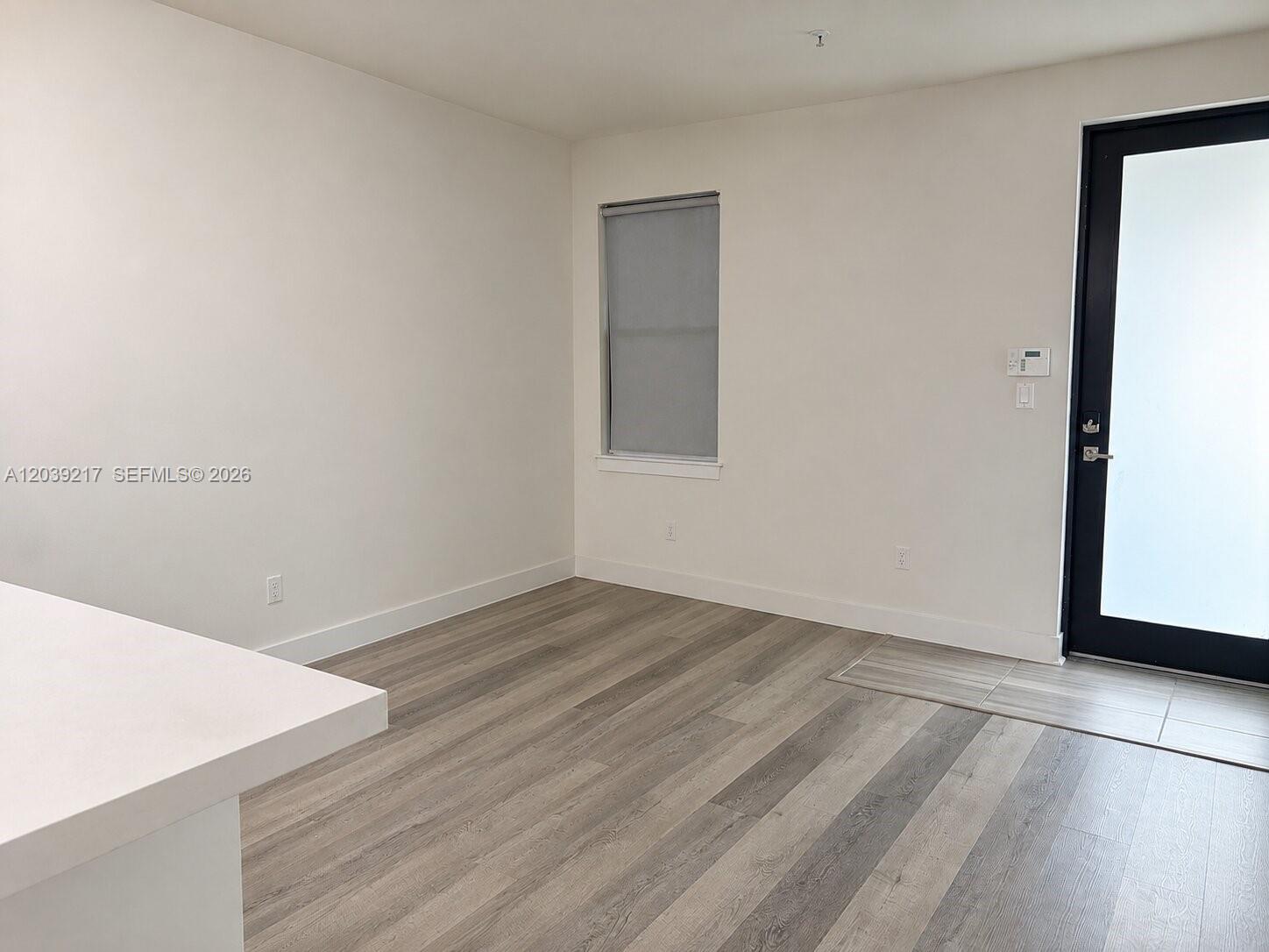 An empty room features light wood-look flooring, white walls, a window, and a glass door — 7809 NW 104th Ave # 5, Doral FL 33178, DORAL, FL