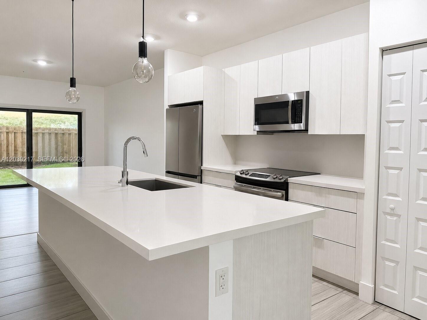 A modern kitchen features a white island with a sink, stainless appliances, and light cabinetry — 7809 NW 104th Ave # 5, Doral FL 33178, DORAL, FL
