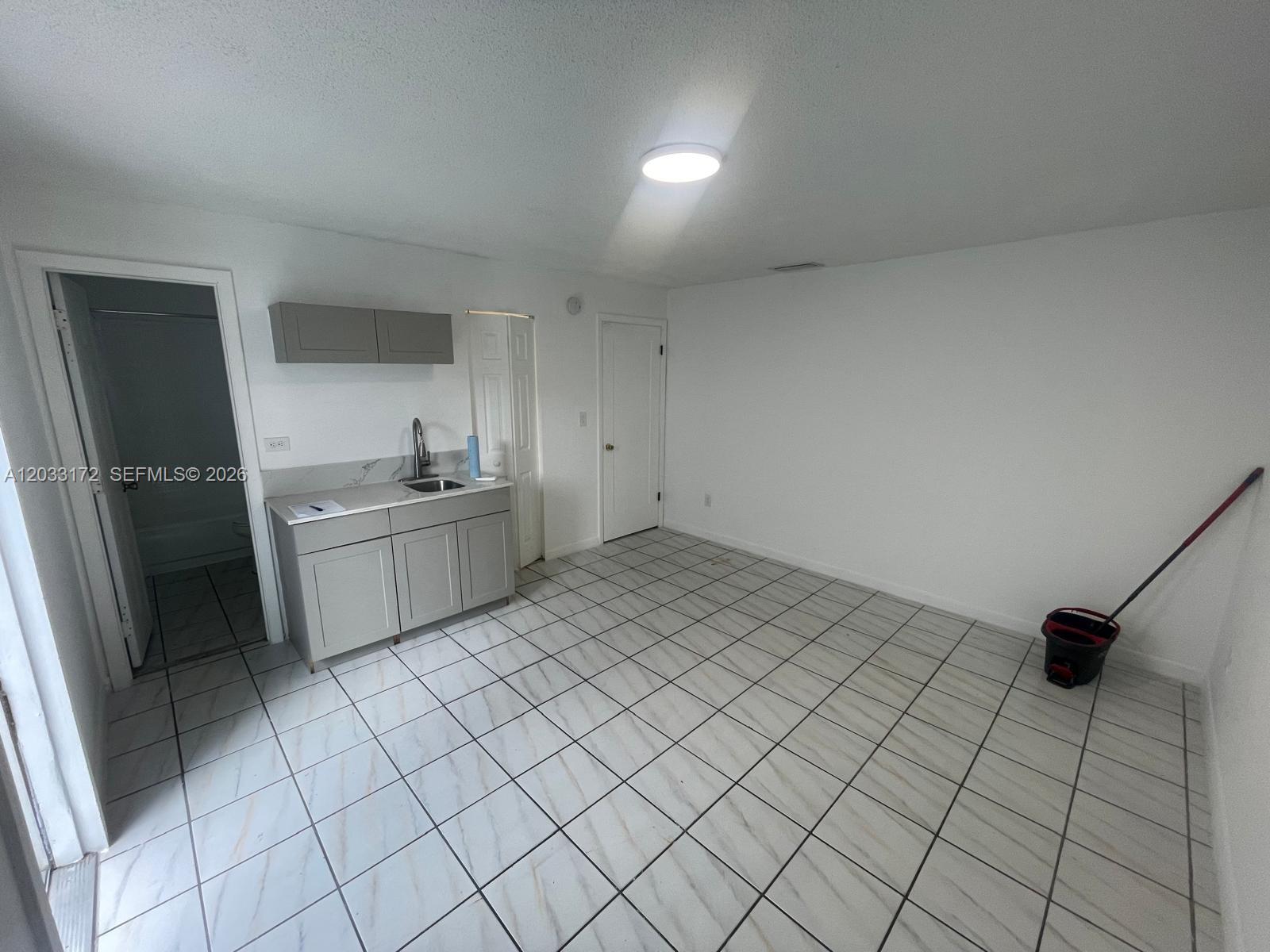 A small room features white tile floors, a kitchenette with gray cabinets, and two doors — 1717 NW 16th St # B, Miami FL 33125, MIAMI, FL