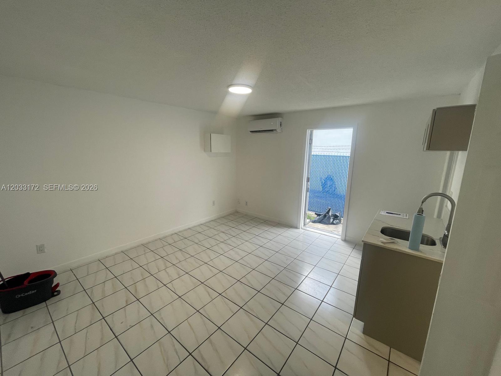 A small, white-walled room features tiled flooring, a kitchenette, and a door leading outside — 1717 NW 16th St # B, Miami FL 33125, MIAMI, FL
