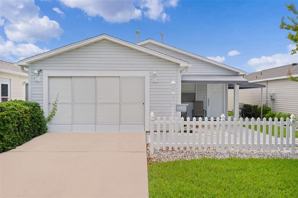 A light gray single-story house features a white picket fence and a concrete driveway — 16933 SE 94TH SUNNYBROOK CIRCLE, THE VILLAGES, FL