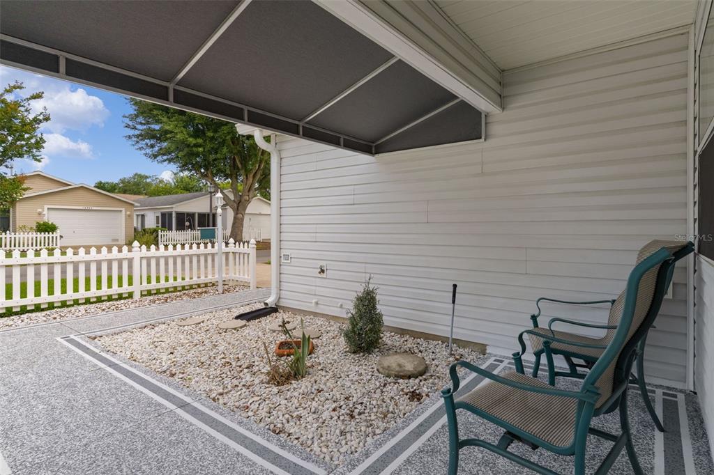A covered patio features a gravel garden bed, white siding, and two metal patio chairs — 16933 SE 94TH SUNNYBROOK CIRCLE, THE VILLAGES, FL
