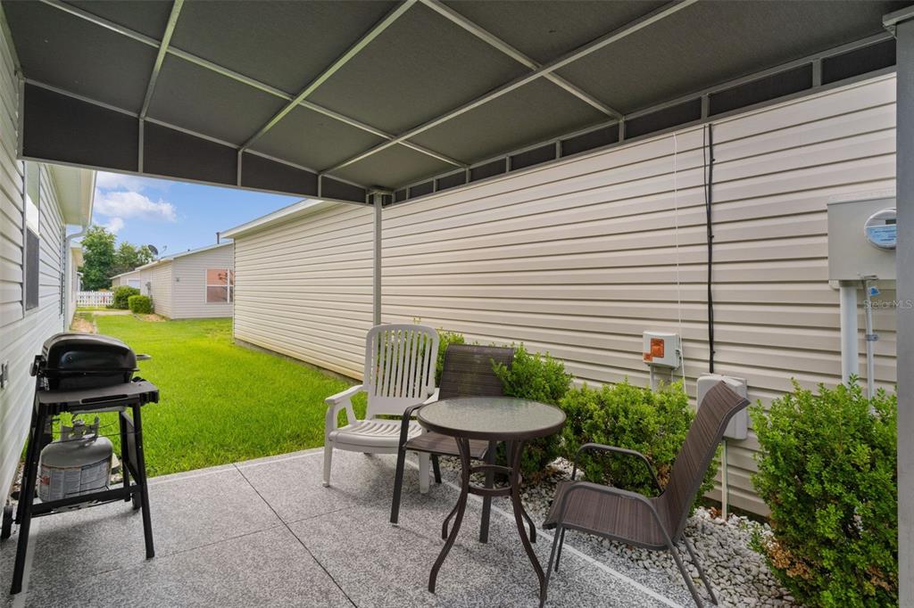 A covered concrete patio features a small table, three chairs, and a propane grill — 16933 SE 94TH SUNNYBROOK CIRCLE, THE VILLAGES, FL