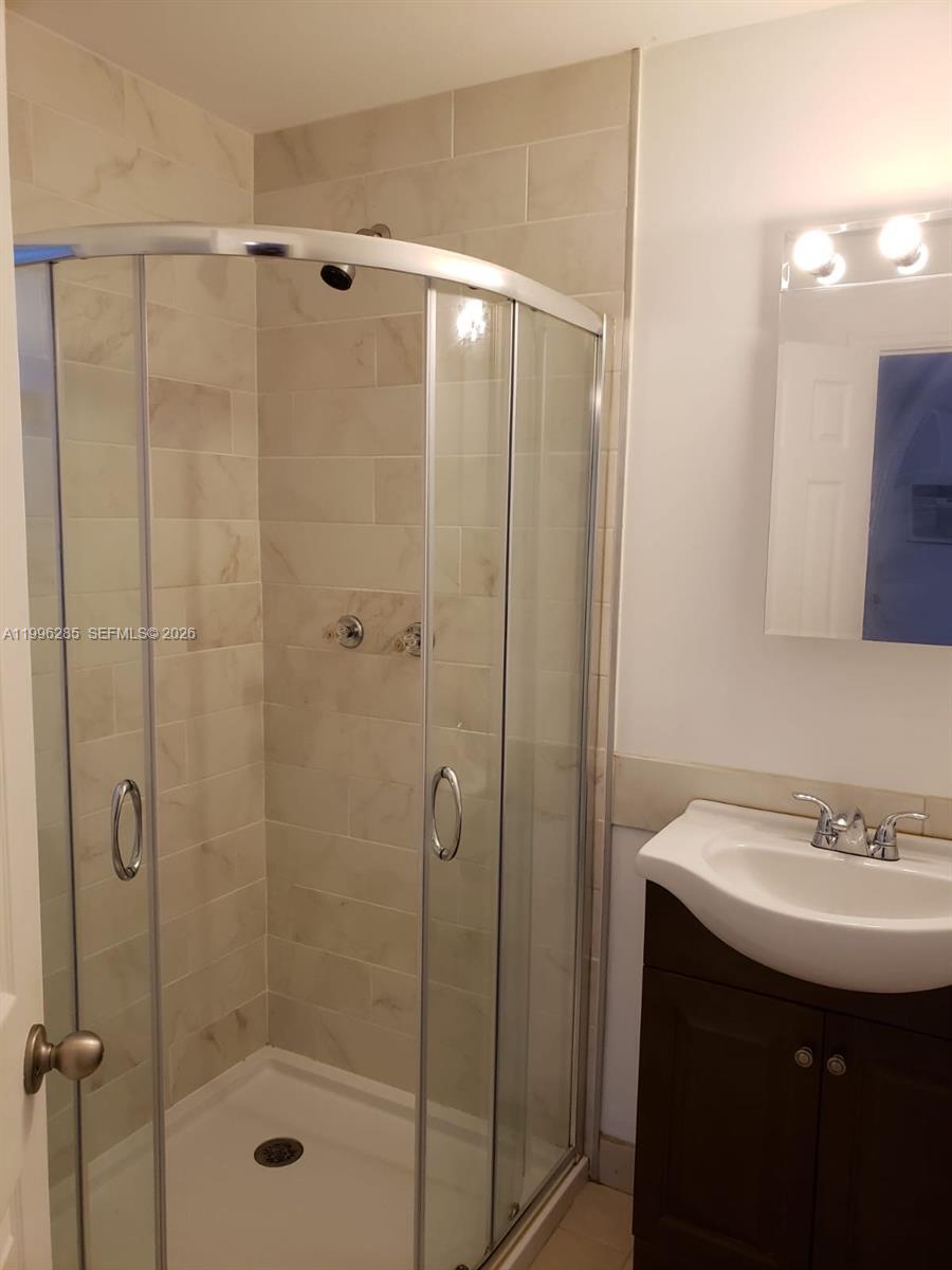 A bathroom features a corner glass shower stall with light-colored tile walls and a vanity — 2481 SW 11 st, Miami FL 33135, MIAMI, FL
