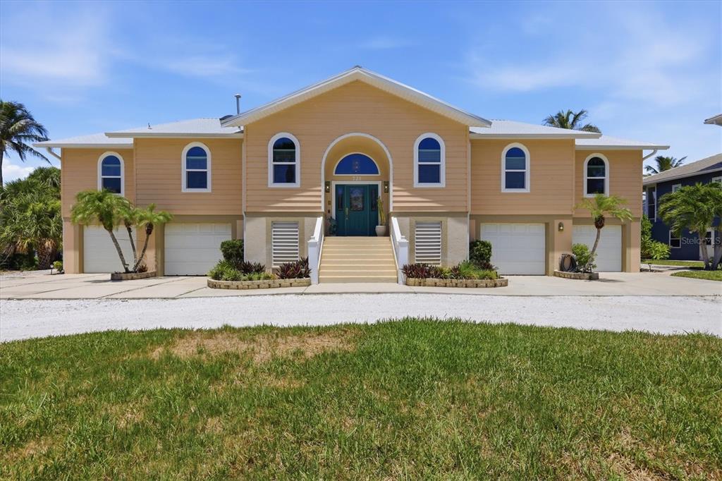 A two-story yellow house with a central staircase, four garage doors, and arched windows — 721 N MANASOTA KEY ROAD, ENGLEWOOD, FL