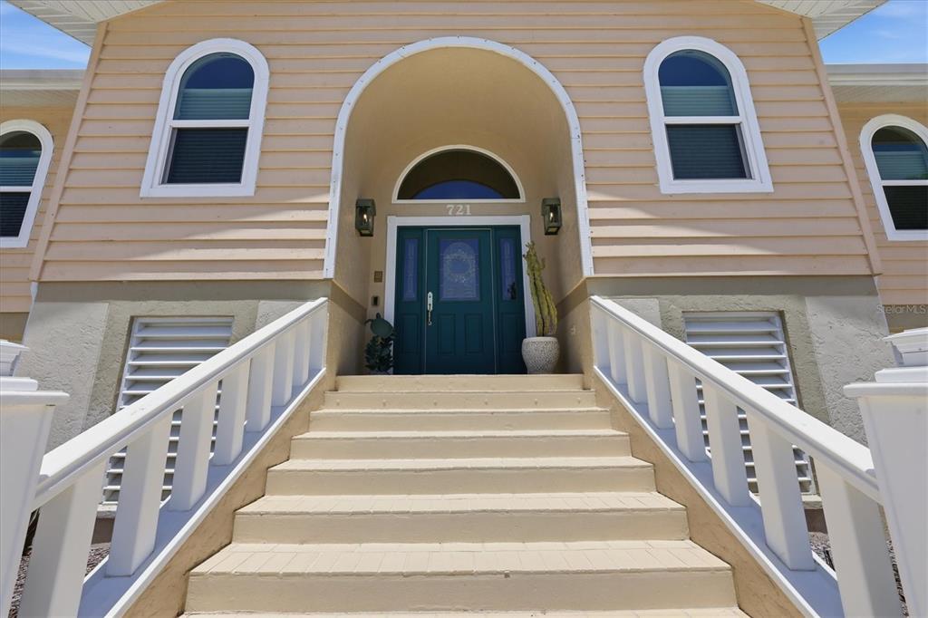 A set of stairs leads to the teal front door of a light-colored house — 721 N MANASOTA KEY ROAD, ENGLEWOOD, FL