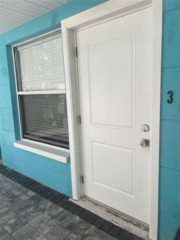 A white door with a deadbolt and knob sits next to a window on a blue wall — 40 82ND AVENUE Unit 3, ST PETERSBURG, FL