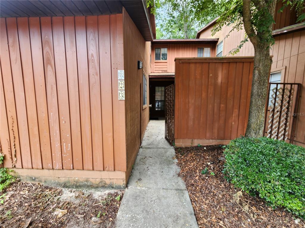 A concrete walkway leads to the entrance of a brown wood-sided building with unit 823 — 823 SW 58TH TERRACE, GAINESVILLE, FL