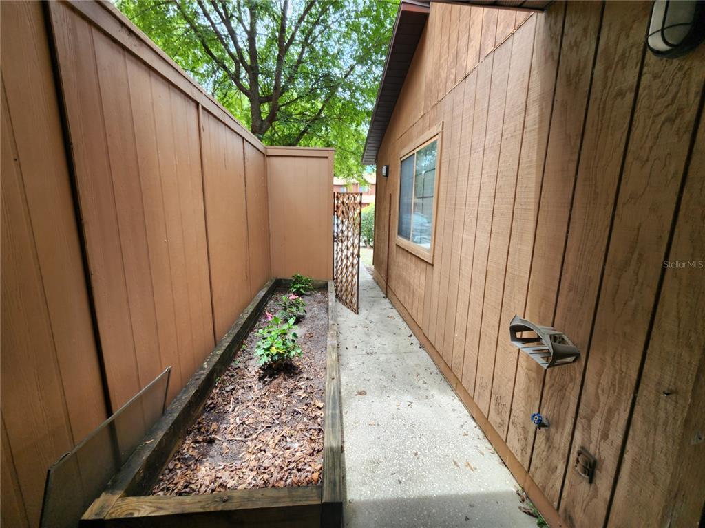 A narrow concrete walkway sits between a wooden fence and a house with a planter — 823 SW 58TH TERRACE, GAINESVILLE, FL
