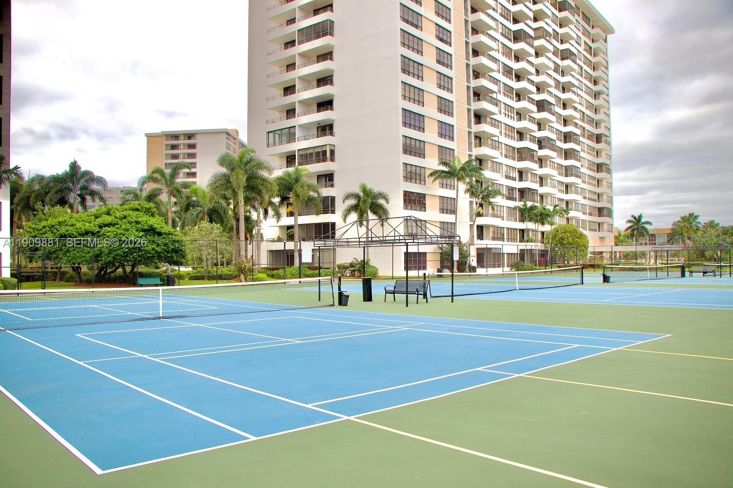 A blue and green tennis court sits in front of a tall residential building — 500 Three Islands Blvd # 920, Hallandale Beach FL 33009, HALLANDALE BEACH, FL