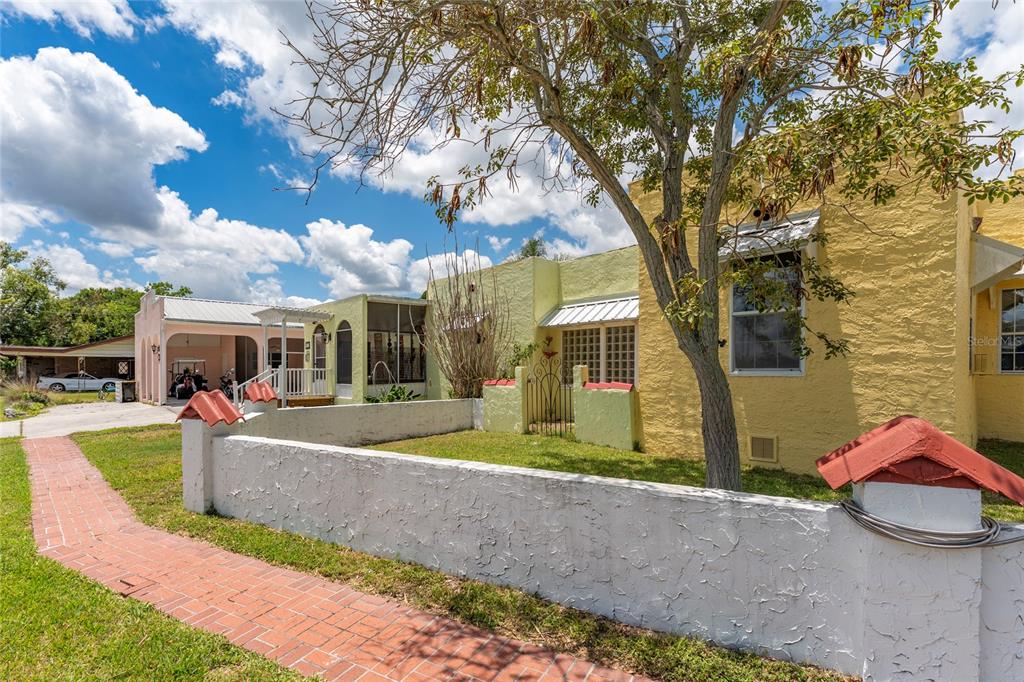 A yellow stucco house with a brick walkway and a low white wall in front — 815 LAKE JESSIE DRIVE, WINTER HAVEN, FL