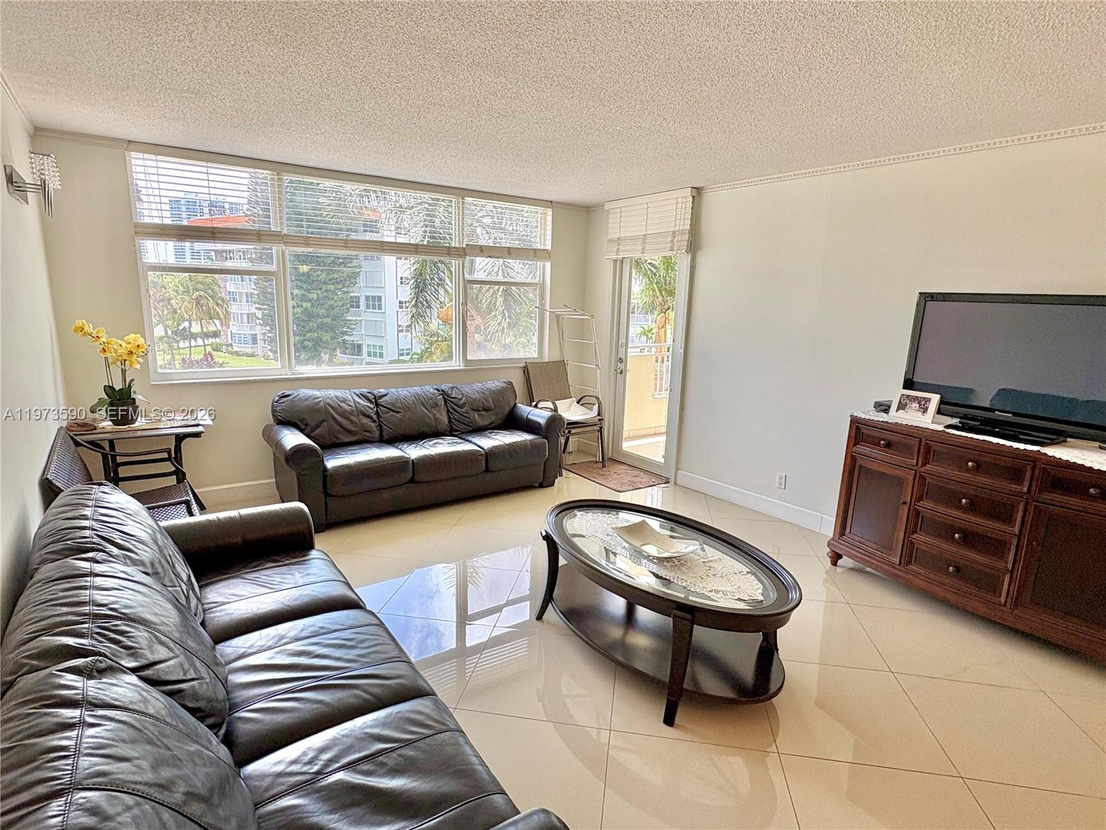A living room features dark leather sofas, a glass coffee table, and large windows — 3180 S Ocean Dr # 221, Hallandale Beach FL 33009, HALLANDALE BEACH, FL