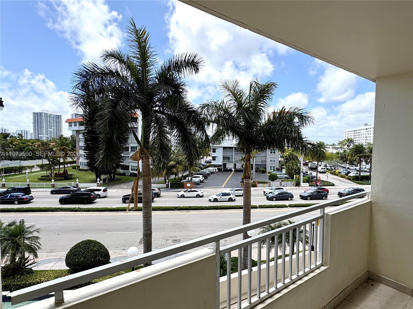 A balcony overlooks a busy multi-lane road with palm trees and surrounding apartment buildings — 3180 S Ocean Dr # 221, Hallandale Beach FL 33009, HALLANDALE BEACH, FL