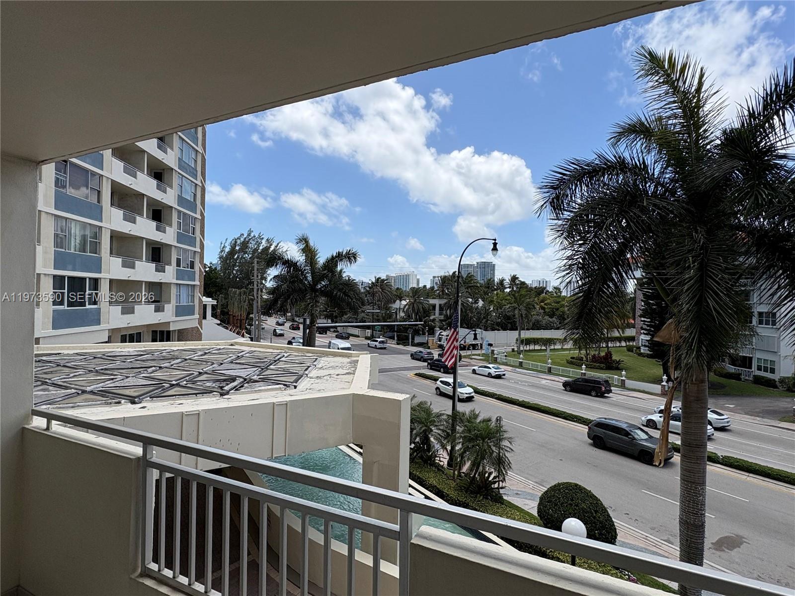 A balcony view overlooks a multi-lane road, palm trees, and a nearby apartment building — 3180 S Ocean Dr # 221, Hallandale Beach FL 33009, HALLANDALE BEACH, FL