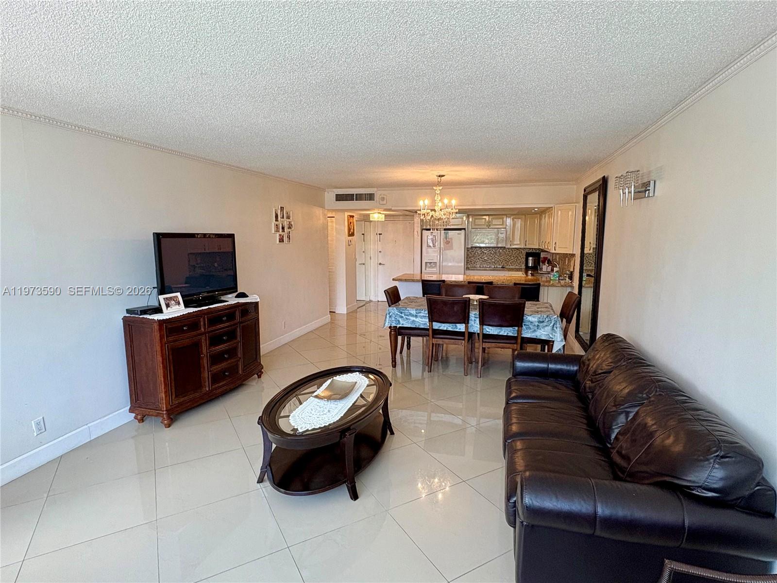 An open-concept living and dining area features tile flooring, a dark leather sofa, and chandelier — 3180 S Ocean Dr # 221, Hallandale Beach FL 33009, HALLANDALE BEACH, FL