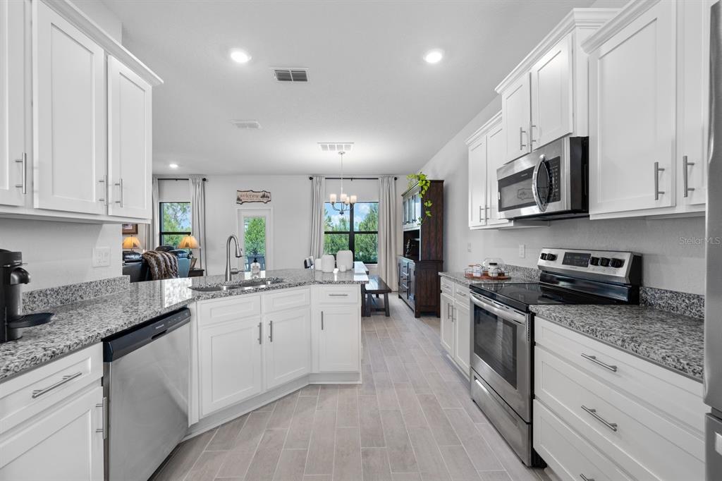 A kitchen with white cabinets, granite countertops, stainless steel appliances, and light wood-look tile flooring — 6107 164TH AVENUE E, PARRISH, FL