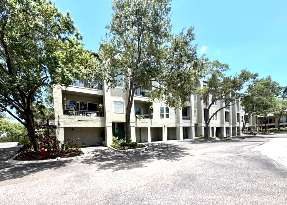 A multi-story apartment building with balconies and ground-level garages sits under a clear sky — 716 PROMENADE PLACE, TAMPA, FL