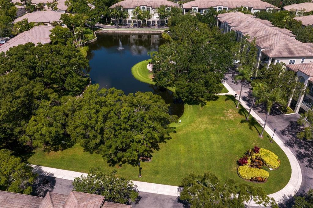 An aerial view shows a pond with a fountain surrounded by apartment buildings and landscaping — 716 PROMENADE PLACE, TAMPA, FL