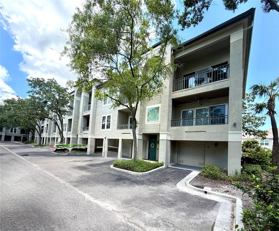 A multi-story residential building features balconies, a green front door, and ground-level garage bays — 716 PROMENADE PLACE, TAMPA, FL