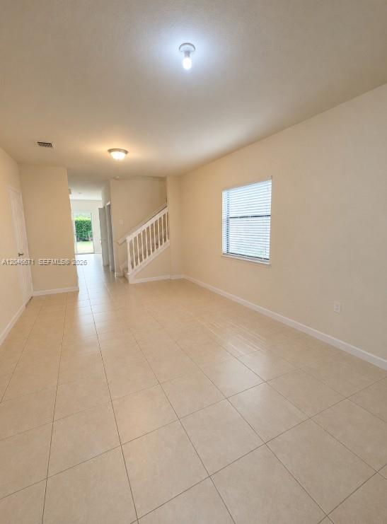 An empty living room features beige tile flooring, a staircase with a white railing, and a window — 8879 SW 227th Ter, Cutler Bay FL 33190, CUTLER BAY, FL