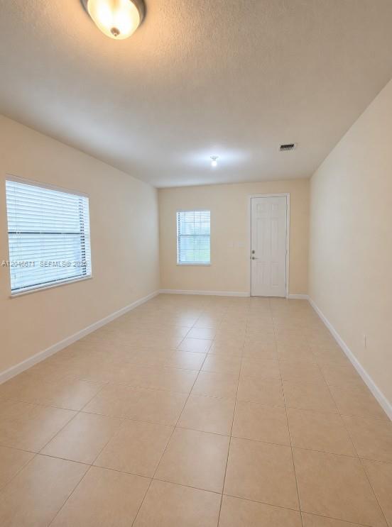 An empty room with beige tile flooring, two windows with blinds, and a white door — 8879 SW 227th Ter, Cutler Bay FL 33190, CUTLER BAY, FL