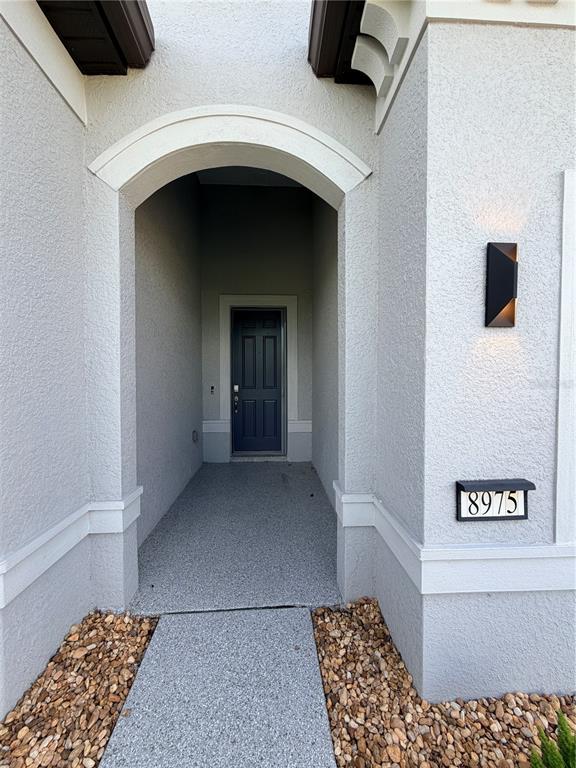 A gray stucco entryway features an arched alcove, a dark front door, and house numbers — 8975 SW 59TH LANE ROAD, OCALA, FL