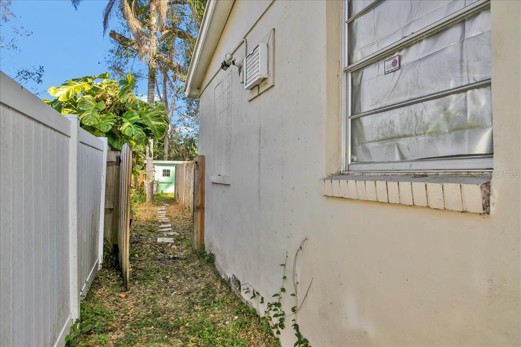 A narrow side yard features a white fence, a stucco house wall, and a small shed — 4017 WATSON ROAD, TAMPA, FL