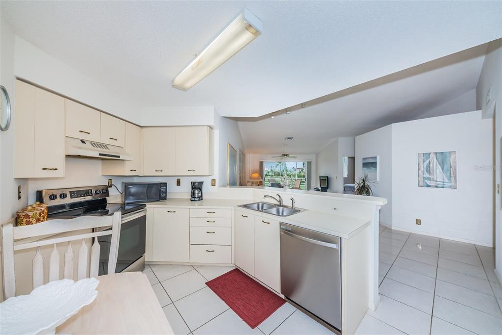 A kitchen with white cabinets, stainless steel appliances, and tile flooring opens to a living area — 6151 BAHIA DEL MAR BOULEVARD UNIT 220, ST PETERSBURG, FL