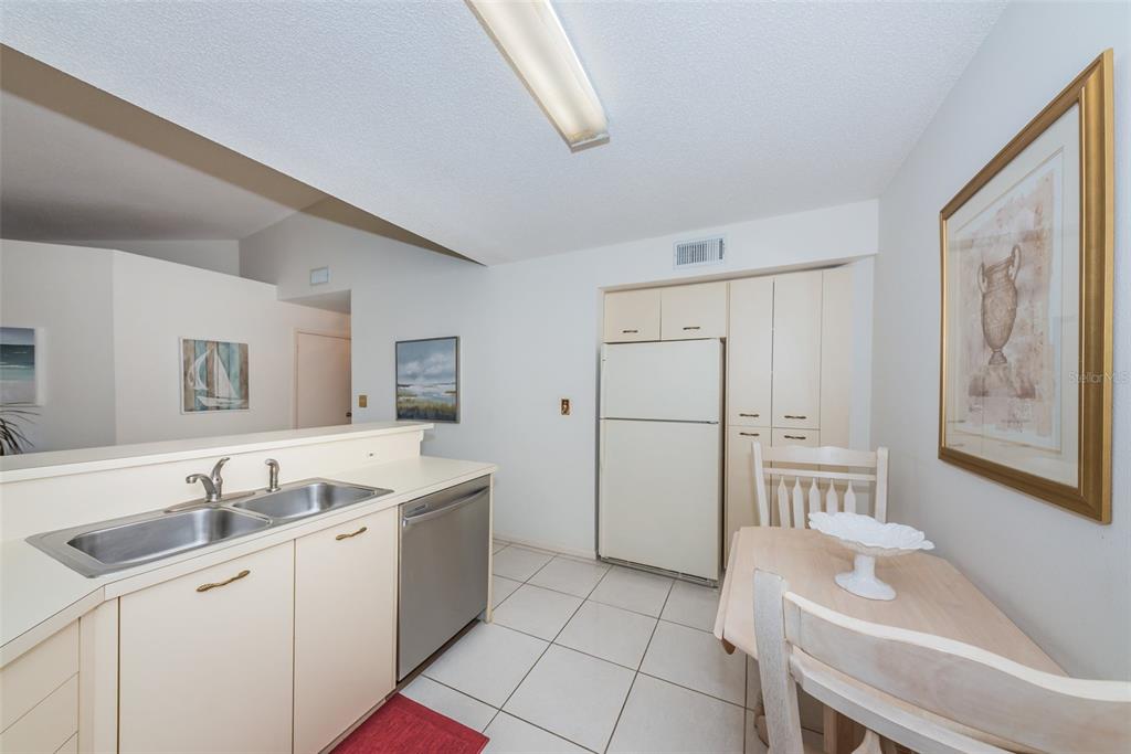 A kitchen with white cabinets, a stainless steel dishwasher, a white refrigerator, and a dining table — 6151 BAHIA DEL MAR BOULEVARD UNIT 220, ST PETERSBURG, FL