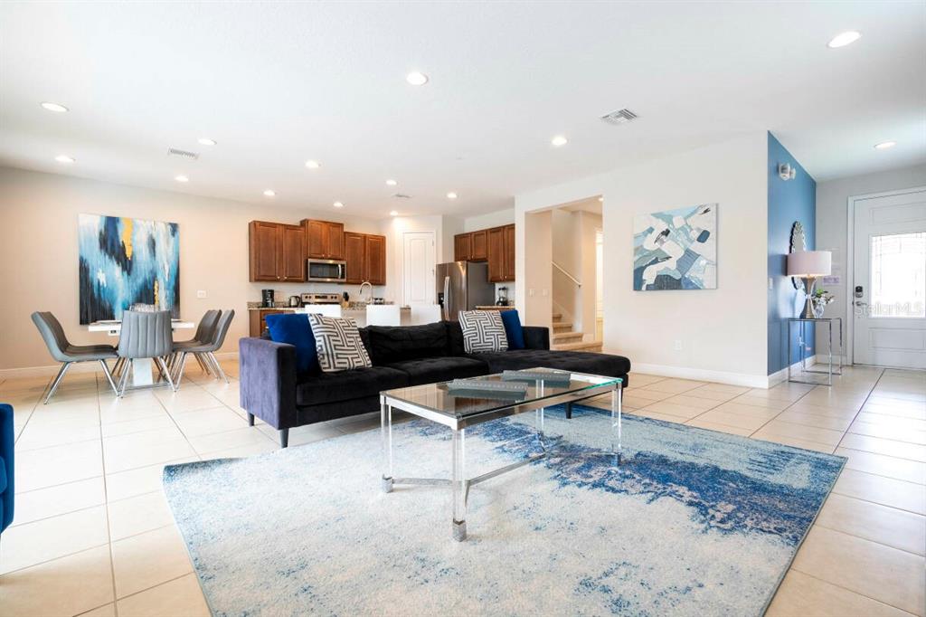 An open-concept living room and kitchen featuring tile floors, a dark sofa, and blue accents — 7479 MARKER AVENUE, KISSIMMEE, FL