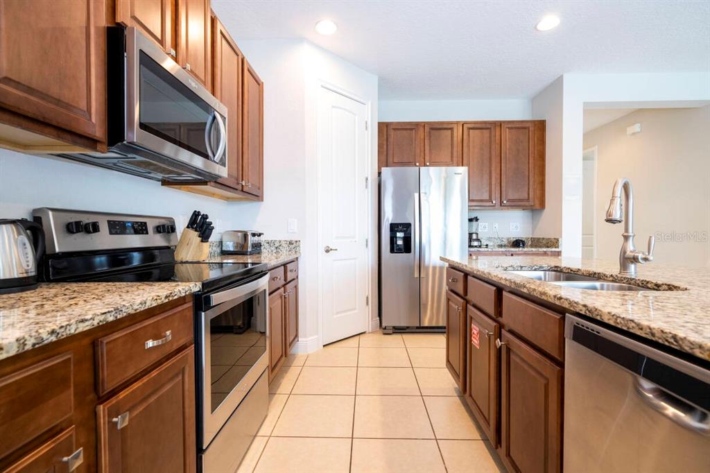 A kitchen features brown cabinets, granite countertops, stainless steel appliances, and tile flooring — 7479 MARKER AVENUE, KISSIMMEE, FL