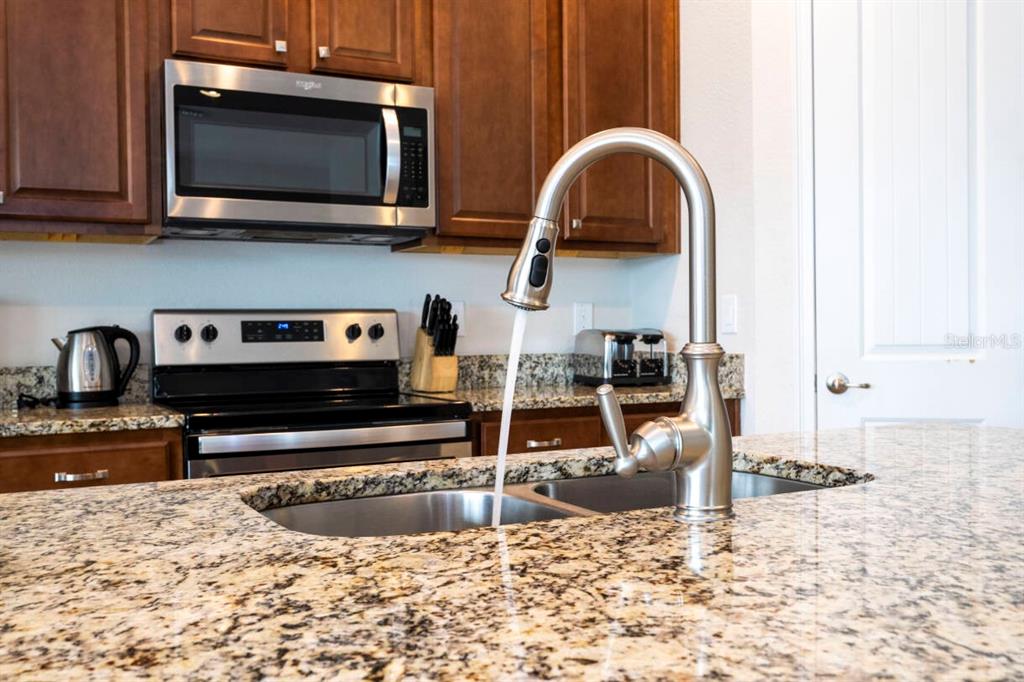 A kitchen island with a stainless steel faucet and granite countertops in front of cabinets — 7479 MARKER AVENUE, KISSIMMEE, FL