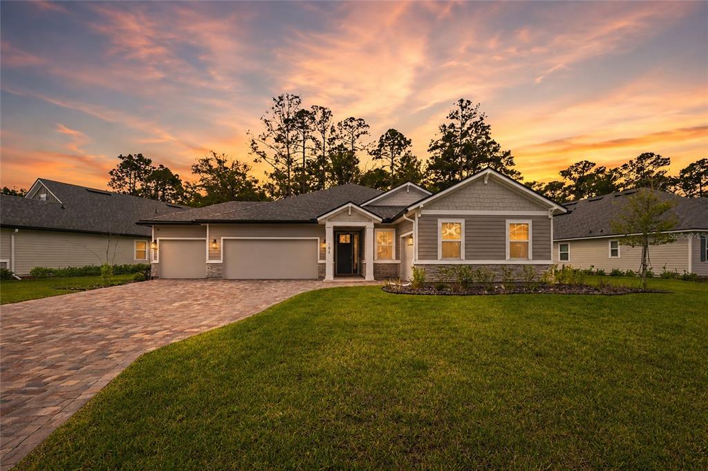 A single-story house with a paved driveway, three-car garage, and gray siding at sunset — 192 GOLDENROD DRIVE, ST AUGUSTINE, FL