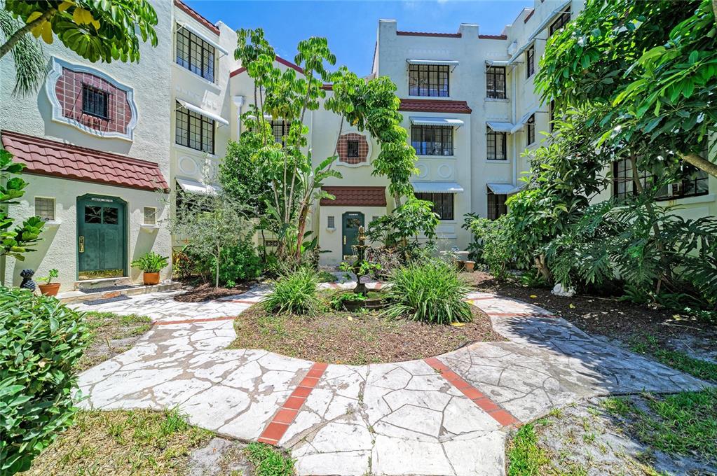 A courtyard with a stone patio, a small fountain, and lush landscaping between apartment buildings — 210 N 17TH STREET W UNIT 14, BRADENTON, FL