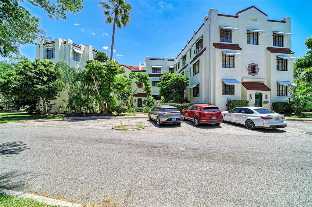A multi-story apartment building with a white facade and red roof accents sits behind parking — 210 N 17TH STREET W UNIT 14, BRADENTON, FL