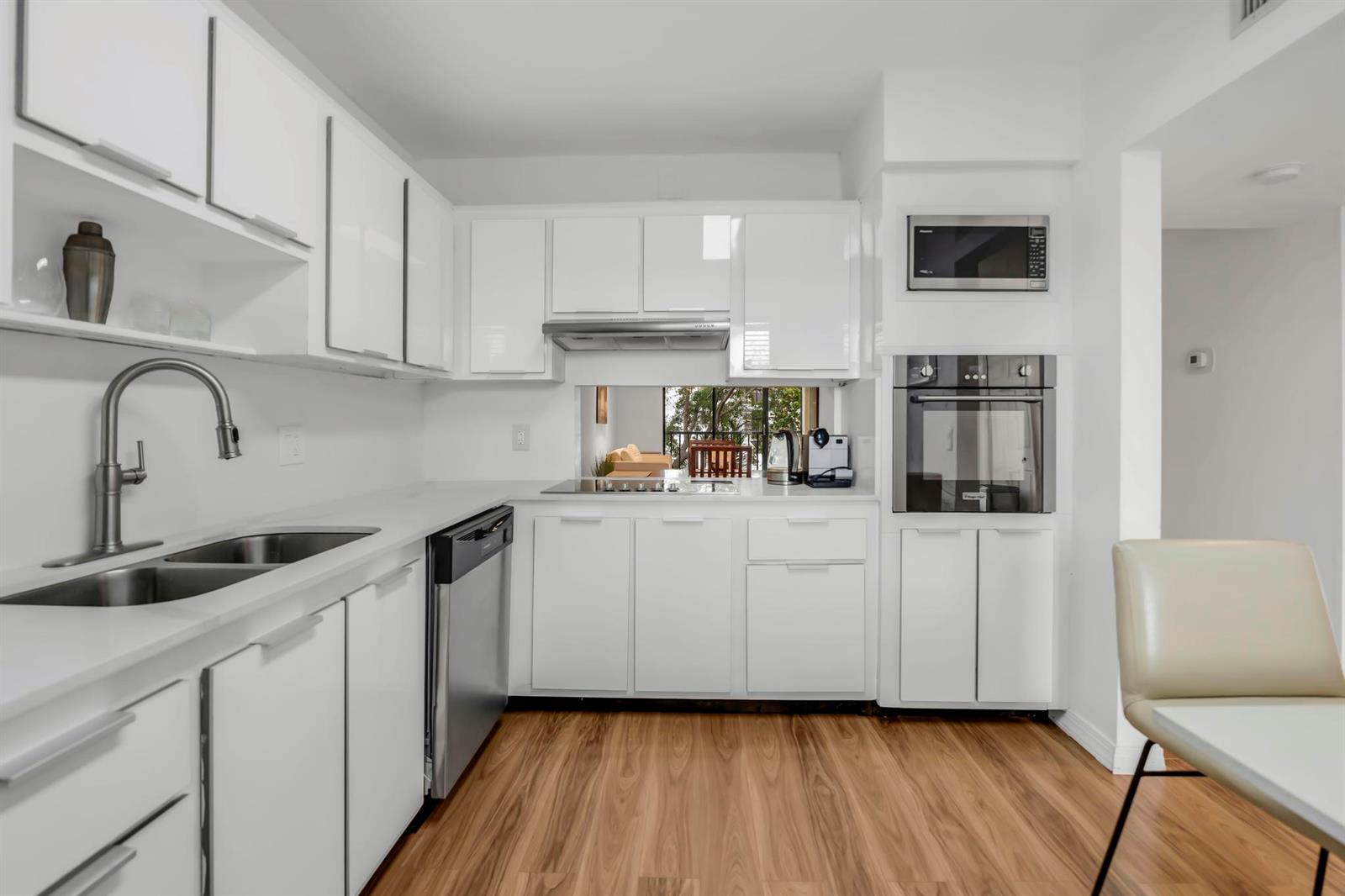 A modern white kitchen features stainless steel appliances, light wood flooring, and a mirrored backsplash — 170 Lakeview Drive # 203, Weston FL 33326, WESTON, FL