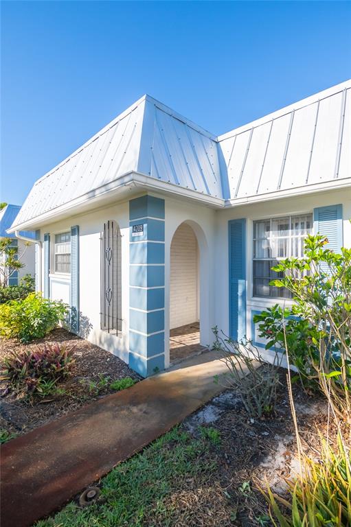 A white house exterior features a metal roof, blue shutters, and a covered entryway — 4209 TAMARGO DRIVE UNIT 4209, NEW PORT RICHEY, FL