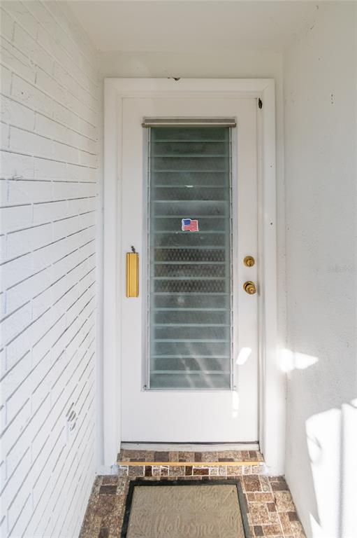 A white front door with a vertical glass louvered window sits between white brick walls — 4209 TAMARGO DRIVE UNIT 4209, NEW PORT RICHEY, FL