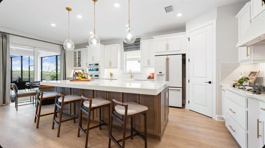 A kitchen with a large wooden island, white cabinets, gold hardware, and three pendant lights — 26619 DOVE DRIVE, PUNTA GORDA, FL