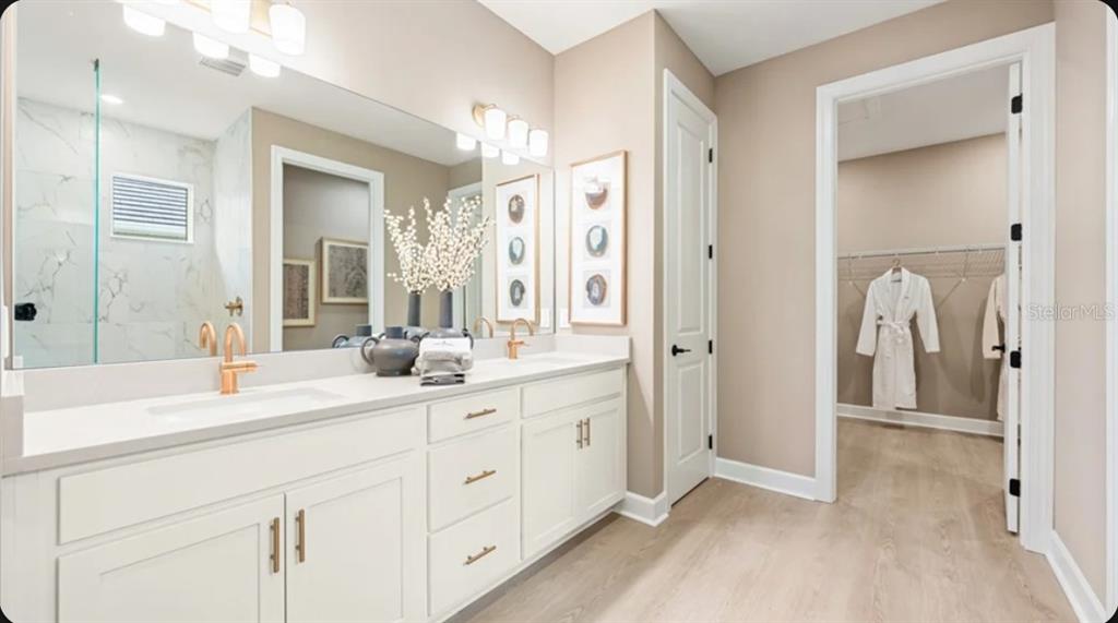 A bathroom with a double vanity, white cabinets, gold fixtures, and an adjacent walk-in closet — 26619 DOVE DRIVE, PUNTA GORDA, FL