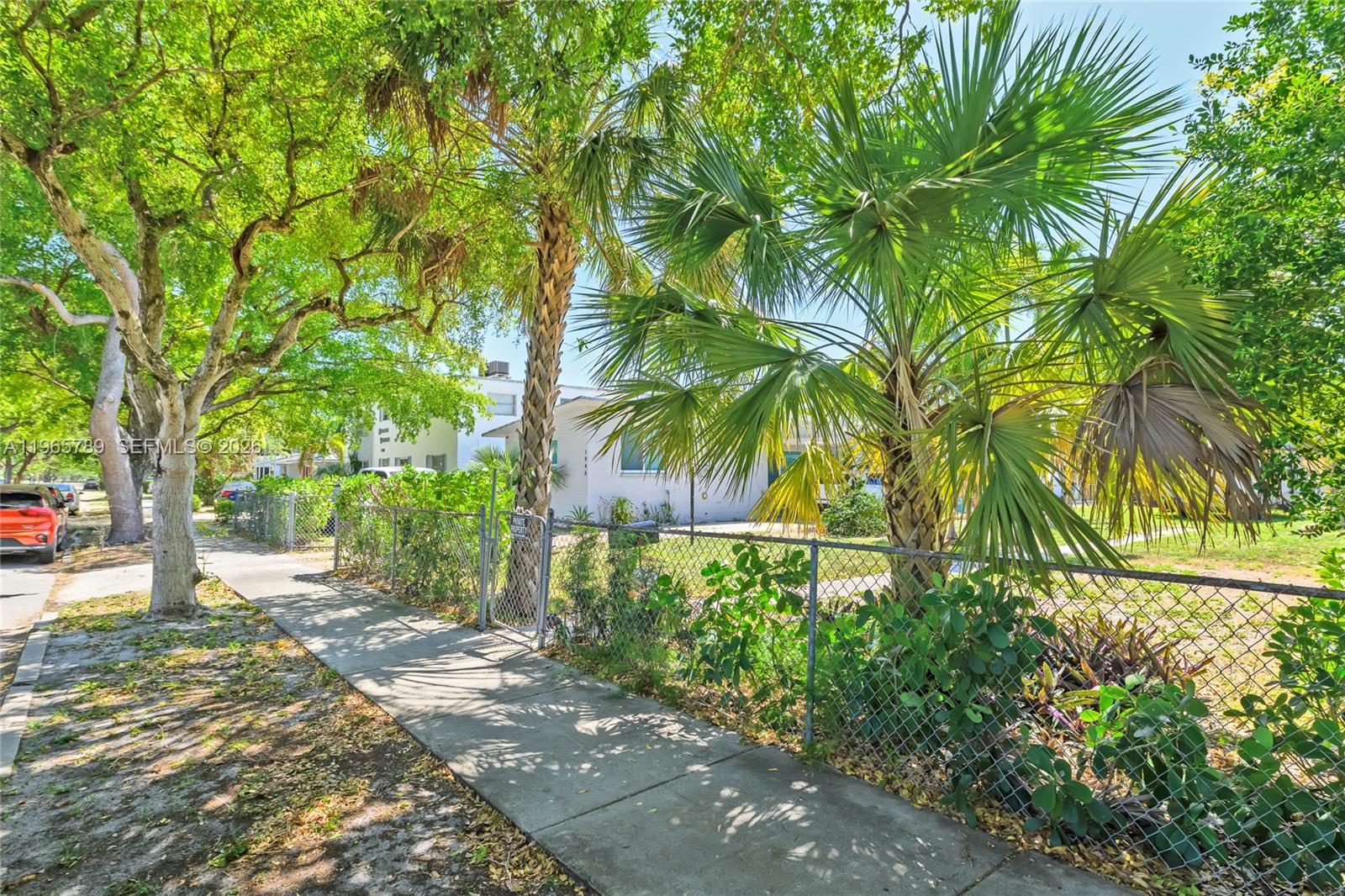 A sidewalk runs alongside a chain-link fence in front of a house with palm trees — 1946 Madison St, Hollywood FL 33020, HOLLYWOOD, FL