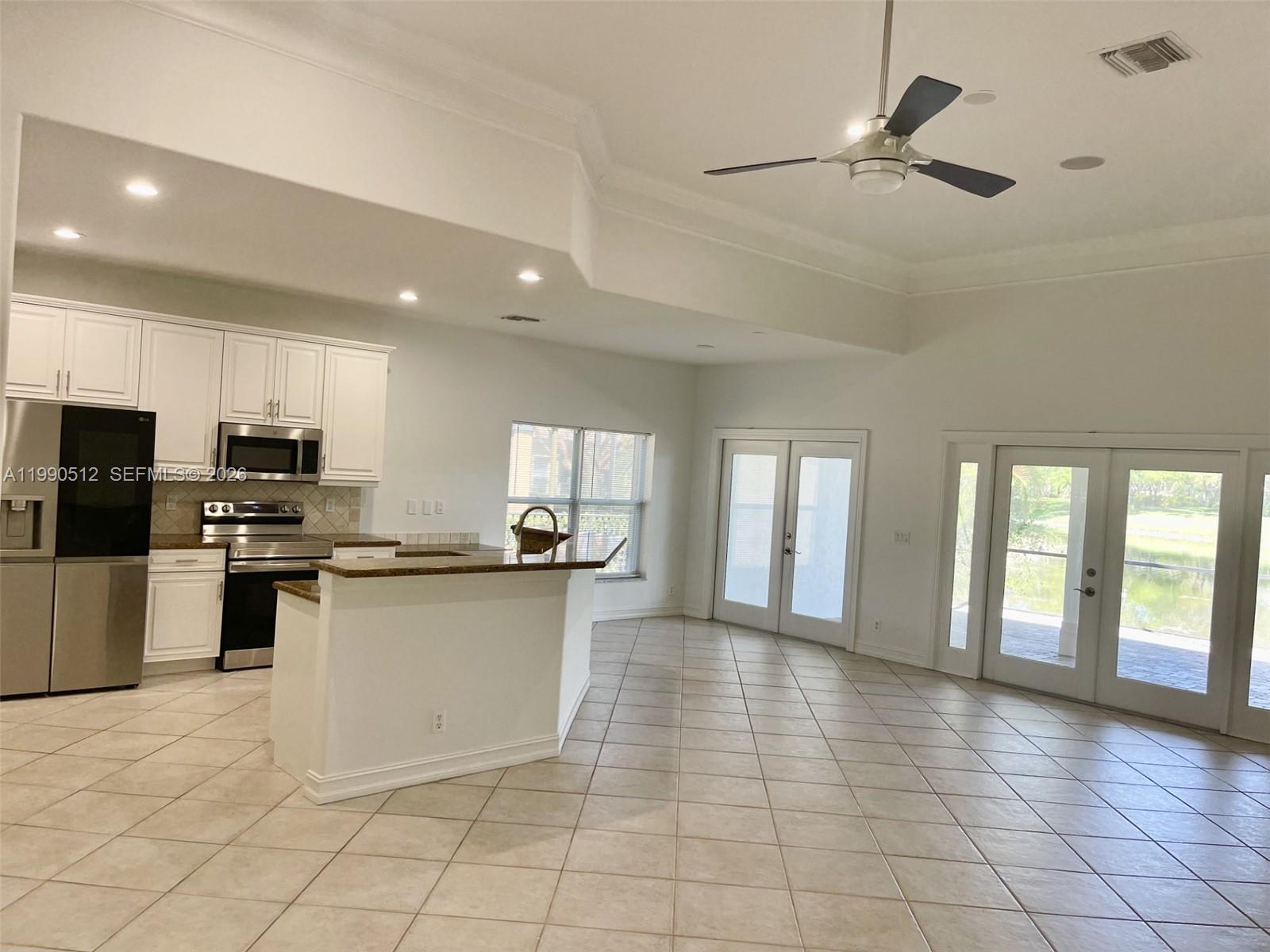A kitchen with white cabinets and a breakfast bar opens into a spacious tiled room — 11289 NW 65th Mnr # 0, Parkland FL 33076, PARKLAND, FL