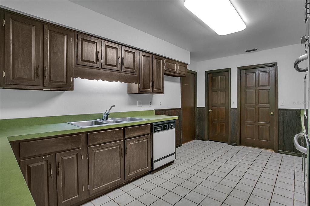 A kitchen features dark wood cabinets, a green countertop, a dishwasher, and tiled flooring — 3629 LAKE BUYNAK ROAD, WINDERMERE, FL