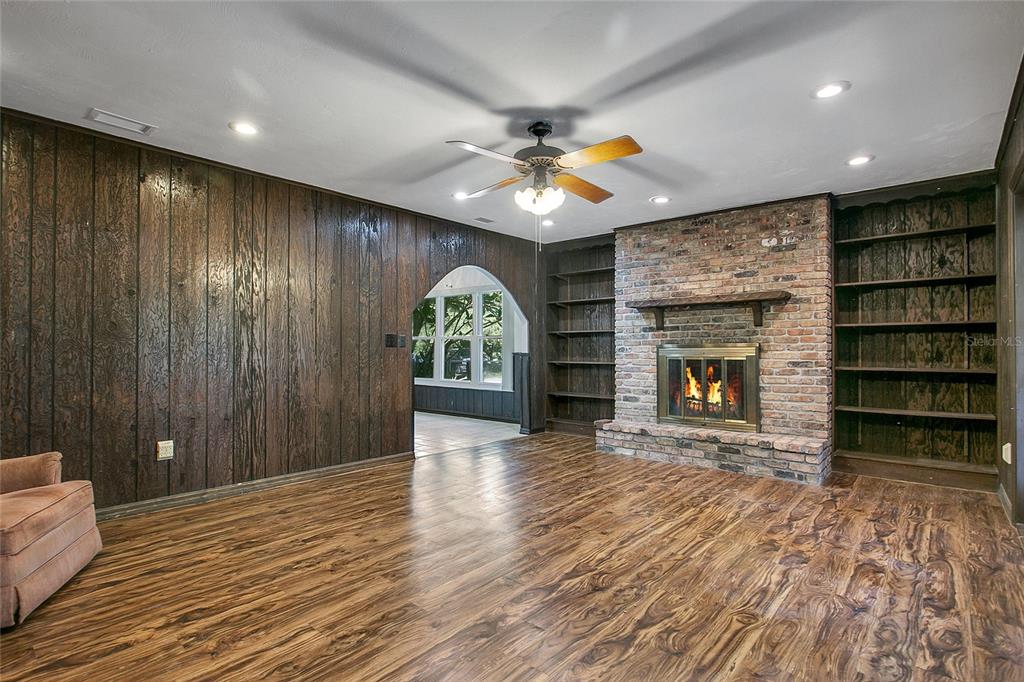A living room features wood-paneled walls, a brick fireplace, built-in shelves, and wood-look flooring — 3629 LAKE BUYNAK ROAD, WINDERMERE, FL