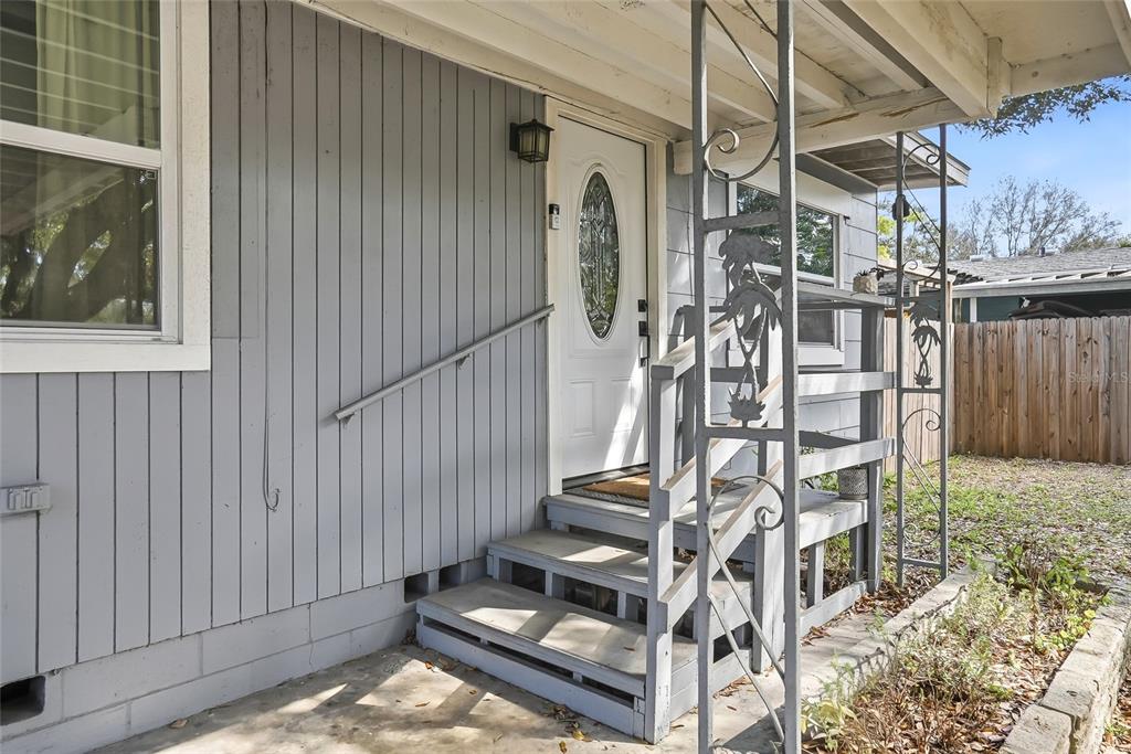 A gray house exterior features a white front door, wooden steps, and decorative metal railings — 1137 40TH STREET, SARASOTA, FL