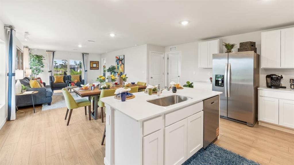 An open-concept kitchen and dining area features white cabinets, stainless steel appliances, and wood flooring — 1517 HARMON DRIVE, PORT CHARLOTTE, FL