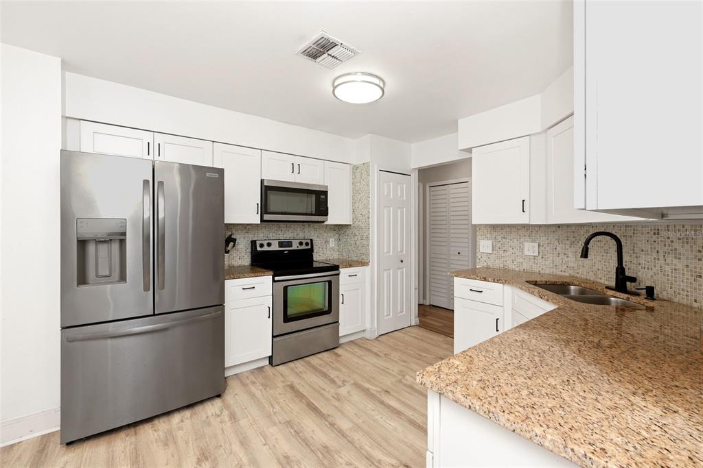 A kitchen features white cabinets, stainless steel appliances, granite countertops, and light wood-look flooring — 10826 SIENA DRIVE, CLERMONT, FL
