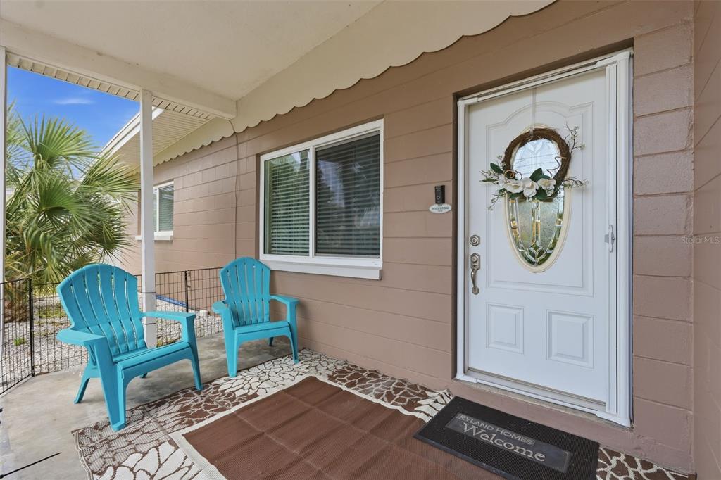 A covered front porch features two blue chairs, a welcome mat, and a white door — 179 E CANAL DRIVE, PALM HARBOR, FL